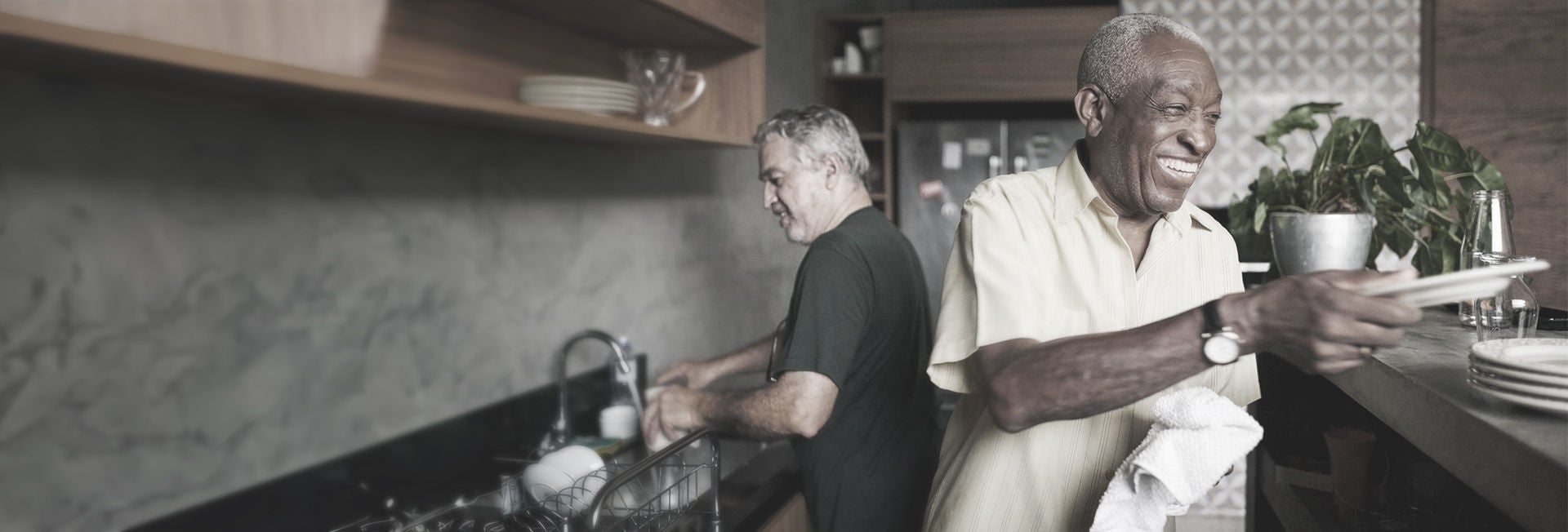 Two senior men washing dishes and smiling in a kitchen