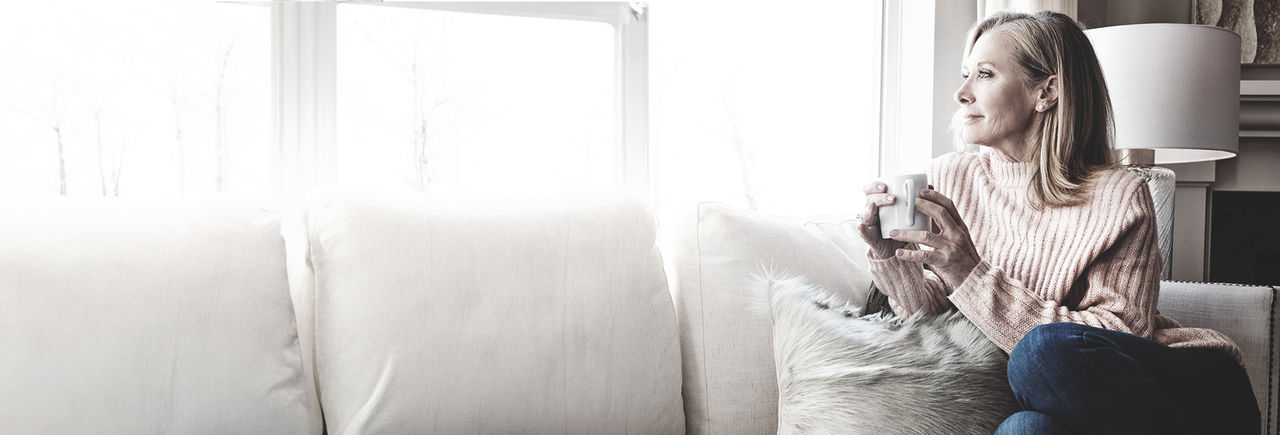 Woman sitting on sofa with coffee, looking out window