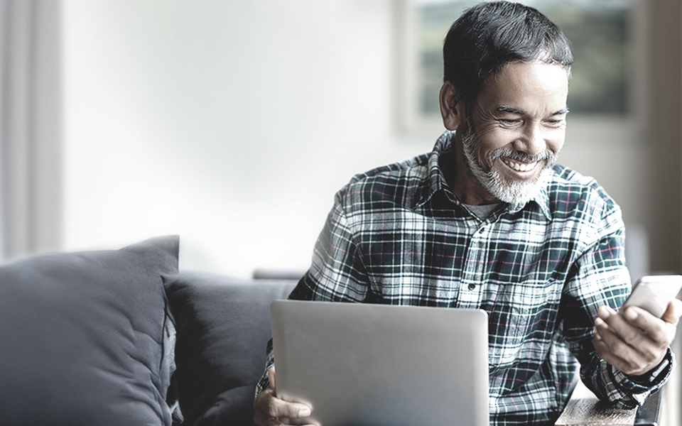 Man smiling while using laptop and smartphone at home