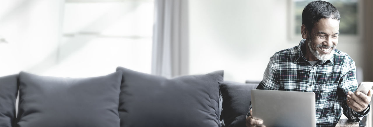 Man smiling while using laptop and smartphone at home